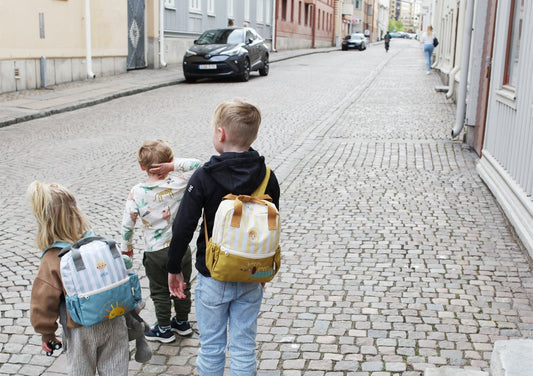 Tre barn med personliga ryggsäckar på väg till förskolan